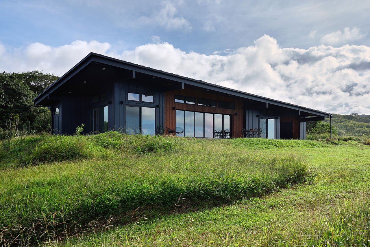 A modern off-grid residence in Hawaii with a distinctive roofline against a lush, misty landscape.